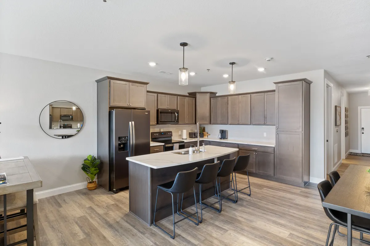 The photo captures a welcoming kitchen with a prominent island countertop, stylish black appliances, wooden cabinetry, and a view of the adjacent dining area. The open layout encourages both cooking and gathering, making it a vibrant hub for entertaining or casual family meals.