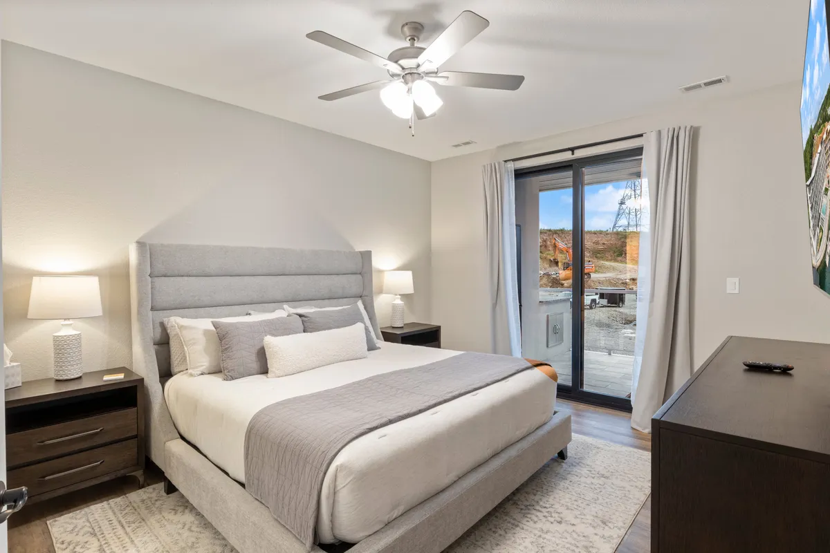 A tranquil bedroom with a comfortable bed, nightstands on either side, tasteful wall art, and sliding glass doors that allow natural light to fill the space. The room feels inviting and perfect for both restful nights and peaceful mornings.