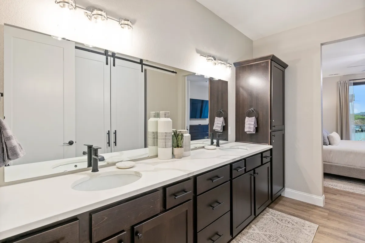 A modern ensuite bathroom featuring a double sink vanity, elegant mirrors, a storage cabinet, and tasteful decorative touches. The space is well-organized and exudes a spa-like calm, ideal for morning and evening self-care routines.