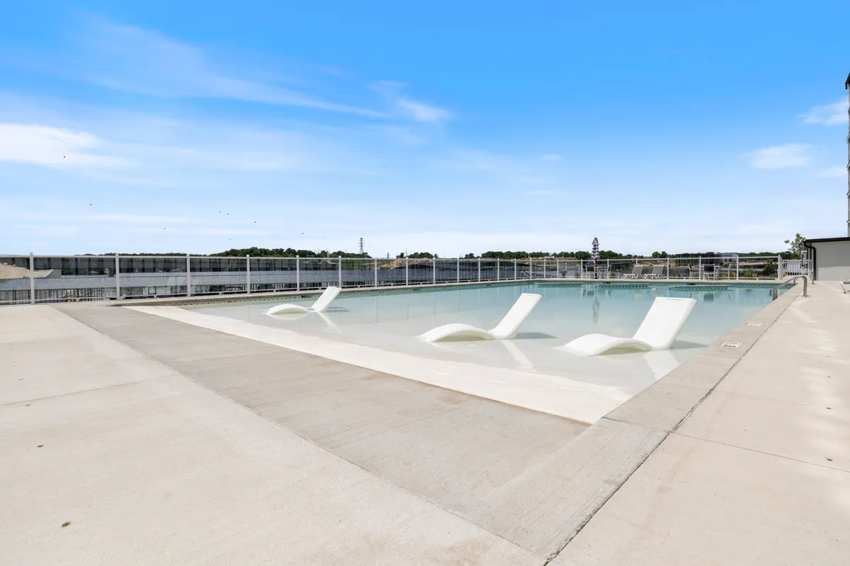A sparkling swimming pool surrounded by comfortable lounge chairs, with a clear sky overhead. The pool area is open, sunlit, and tranquil, creating the ultimate spot for swimming, sunbathing, or gathering with friends on a warm afternoon.