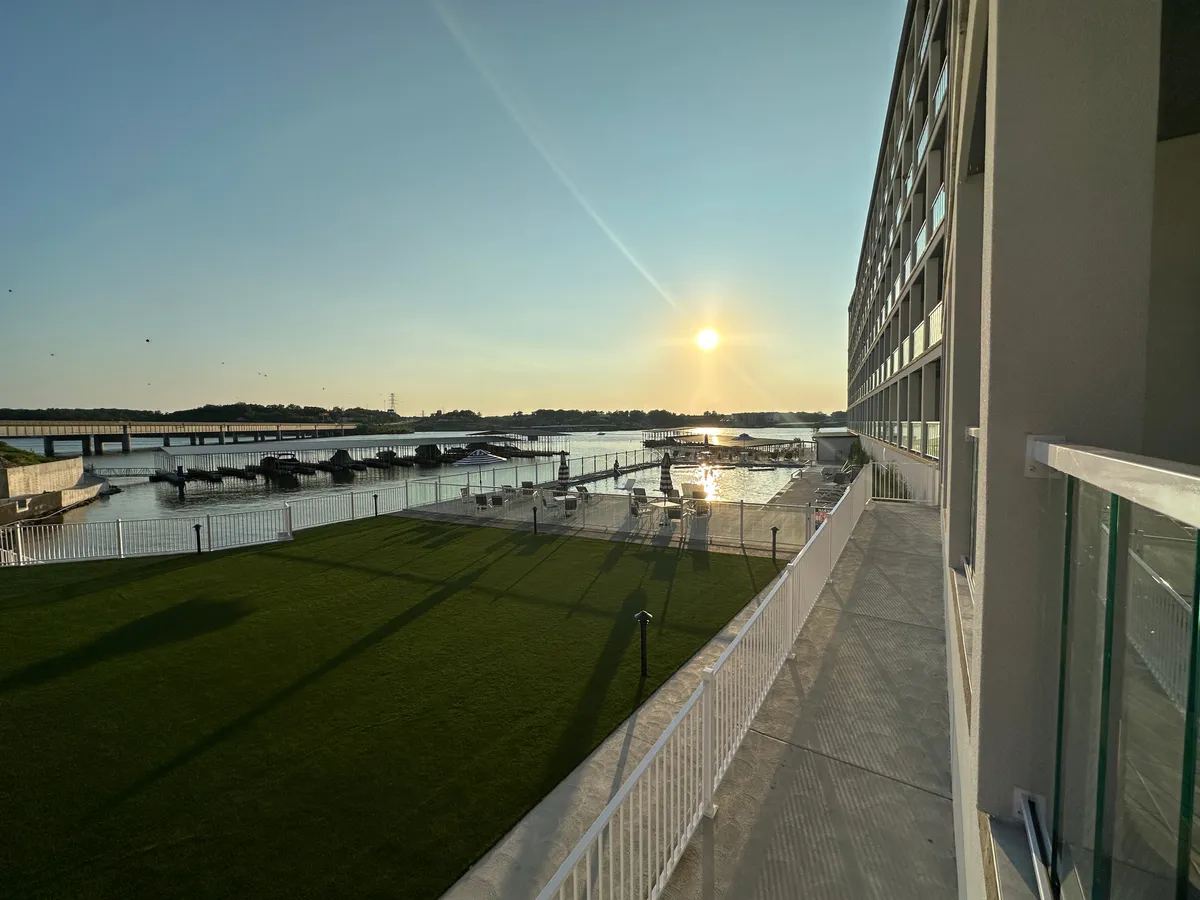 A tranquil scene of sunset over the water, featuring a marina with boats, a green lawn, and a modern building. The image embodies the spirit of boating and water activities, with the marina inviting residents to enjoy boat slip rentals and lake adventures.