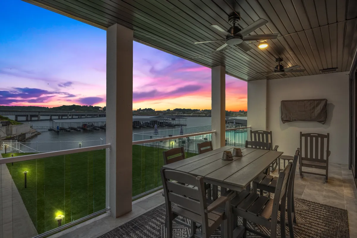 The image showcases a serene waterfront setting at sunset, with a spacious outdoor dining table set on a green lawn overlooking the water. The warm glow of the evening sky reflects off the water, inviting guests to gather for alfresco meals, socializing, and relaxation in a peaceful environment.