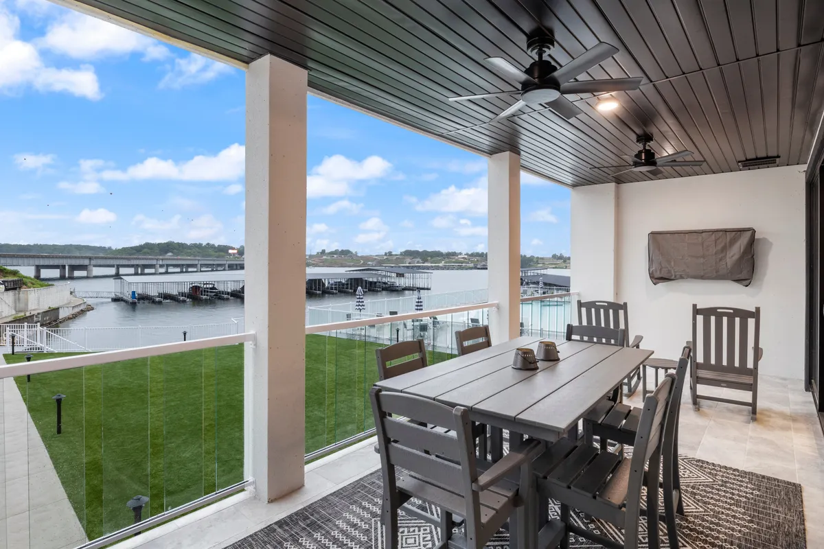 An outdoor dining area with a table set for a meal, overlooking the tranquil water. Ceiling fans and comfortable seating create a welcoming space for al fresco dining and social gatherings with friends.