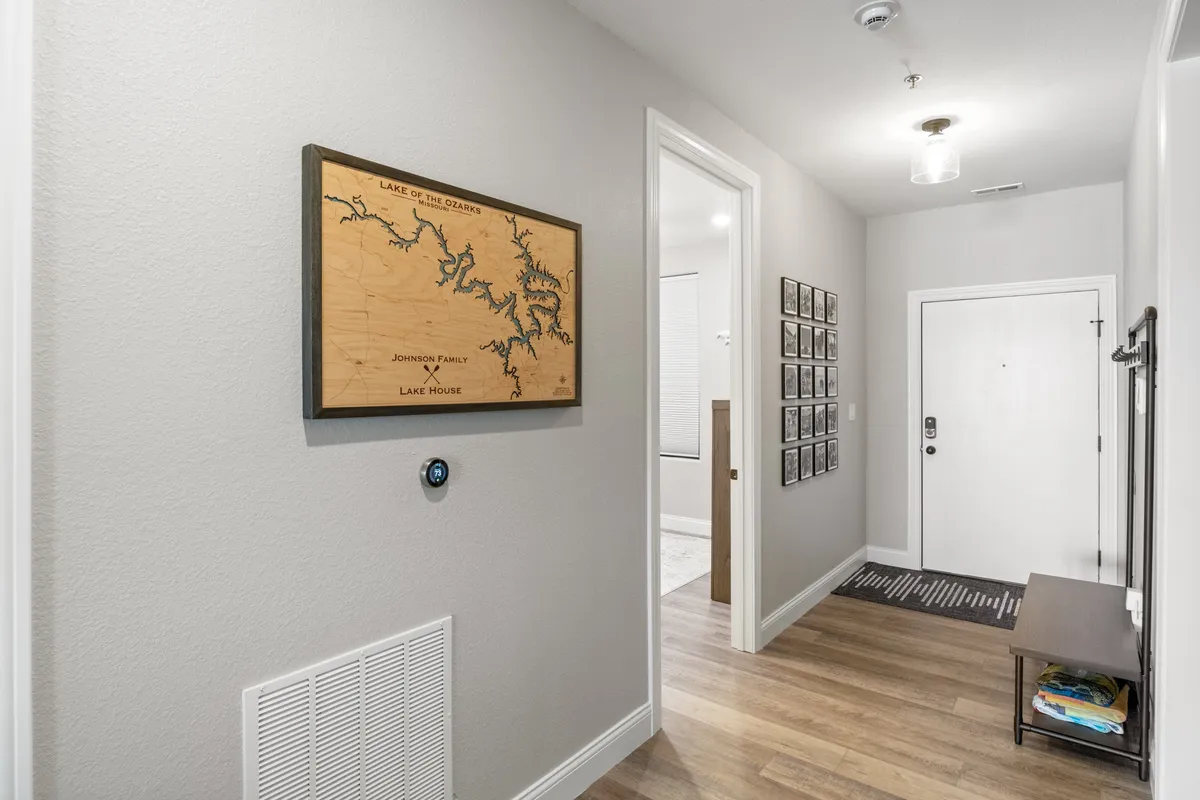 An inviting entryway with a wooden map of Lake of the Ozarks and a gallery of framed photographs. The front door is visible, setting a welcoming tone and emphasizing both personalization and local connection.