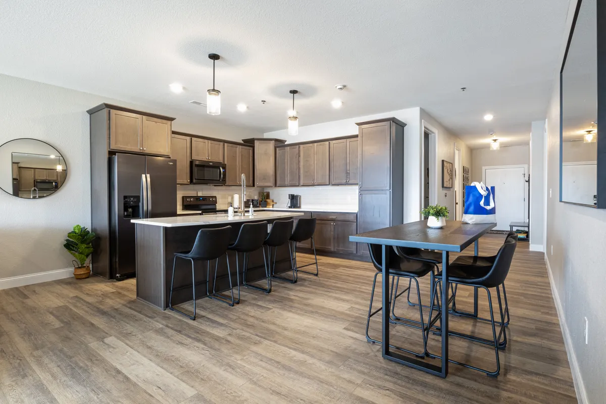 A bright, modern kitchen with a central island, sleek black bar stools, a circular mirror, and high-end appliances. The design is welcoming and practical, perfect for preparing meals and gathering with friends or family.