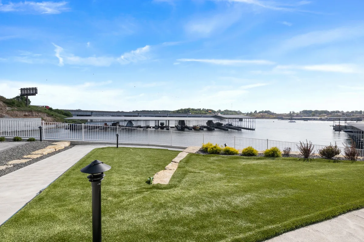 A tranquil waterfront view with a green lawn, dock area, and landscaped garden along the shore of Lake of the Ozarks. The setting is peaceful and open, inviting guests to enjoy nature, have a picnic, or explore nearby walking trails.