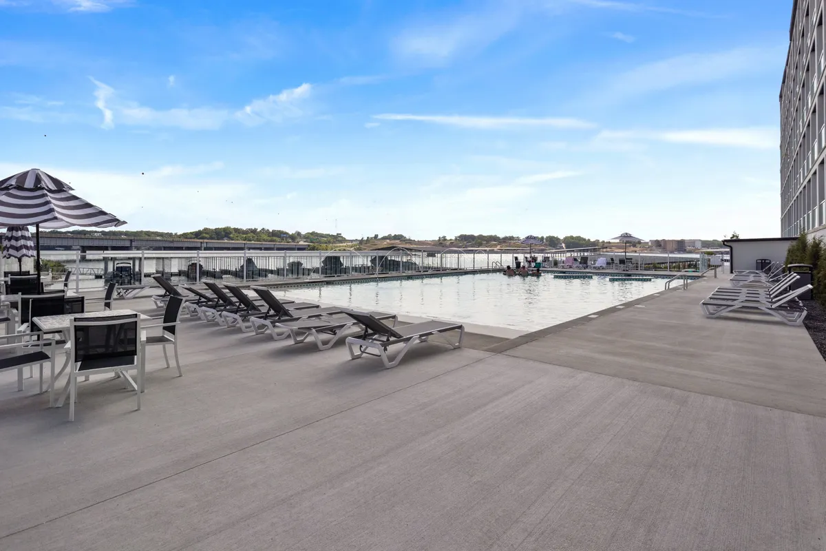 A vibrant outdoor pool area featuring lounge chairs, umbrellas, and a sparkling pool set against a natural backdrop. The scene hints at leisure, socializing, and sun-soaked relaxation, perfect for both quiet swims and lively gatherings.